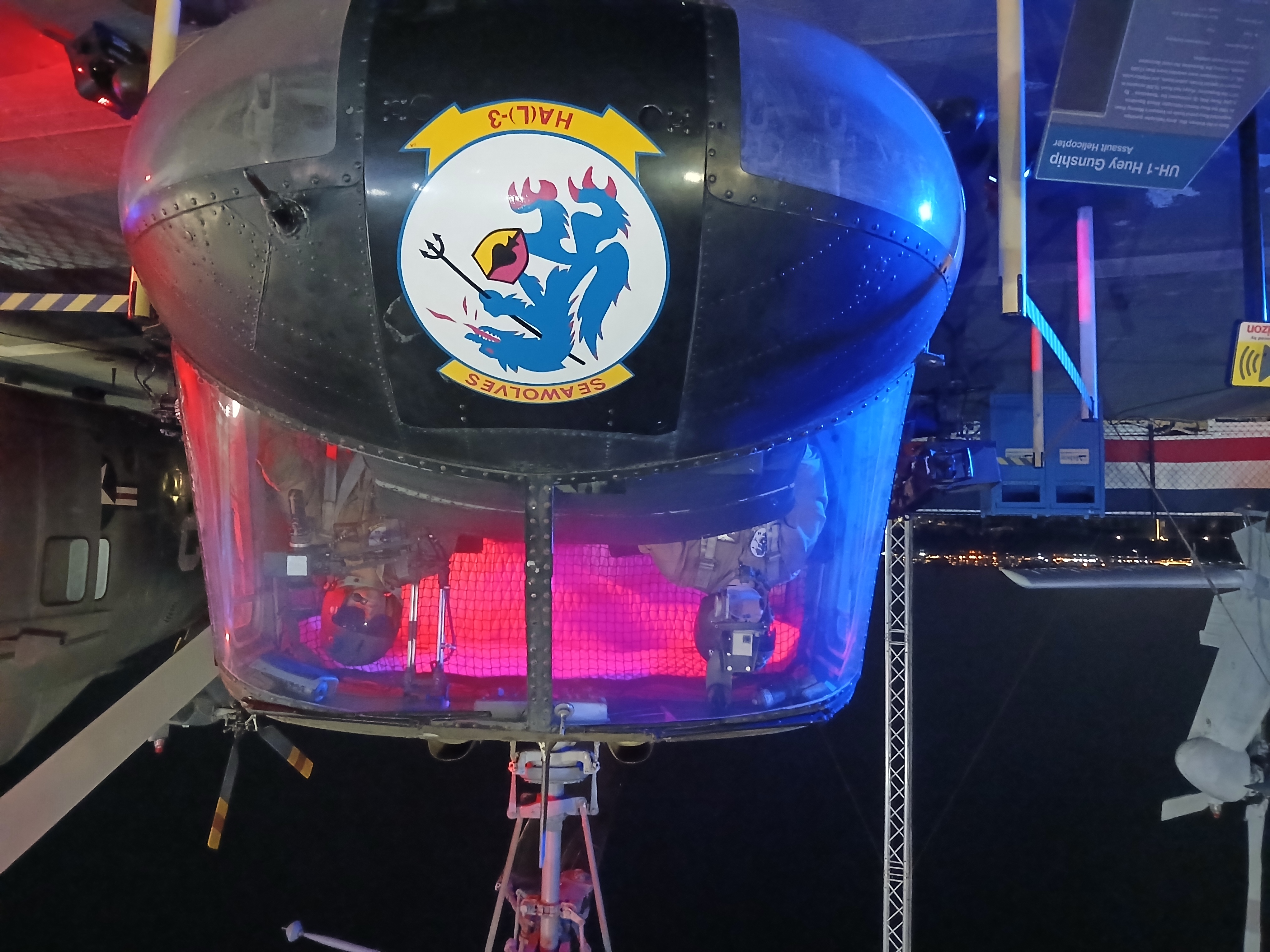 A dark helicopter pictured through the windshield. Two mannequins stare out at the camera from the pilot seats.