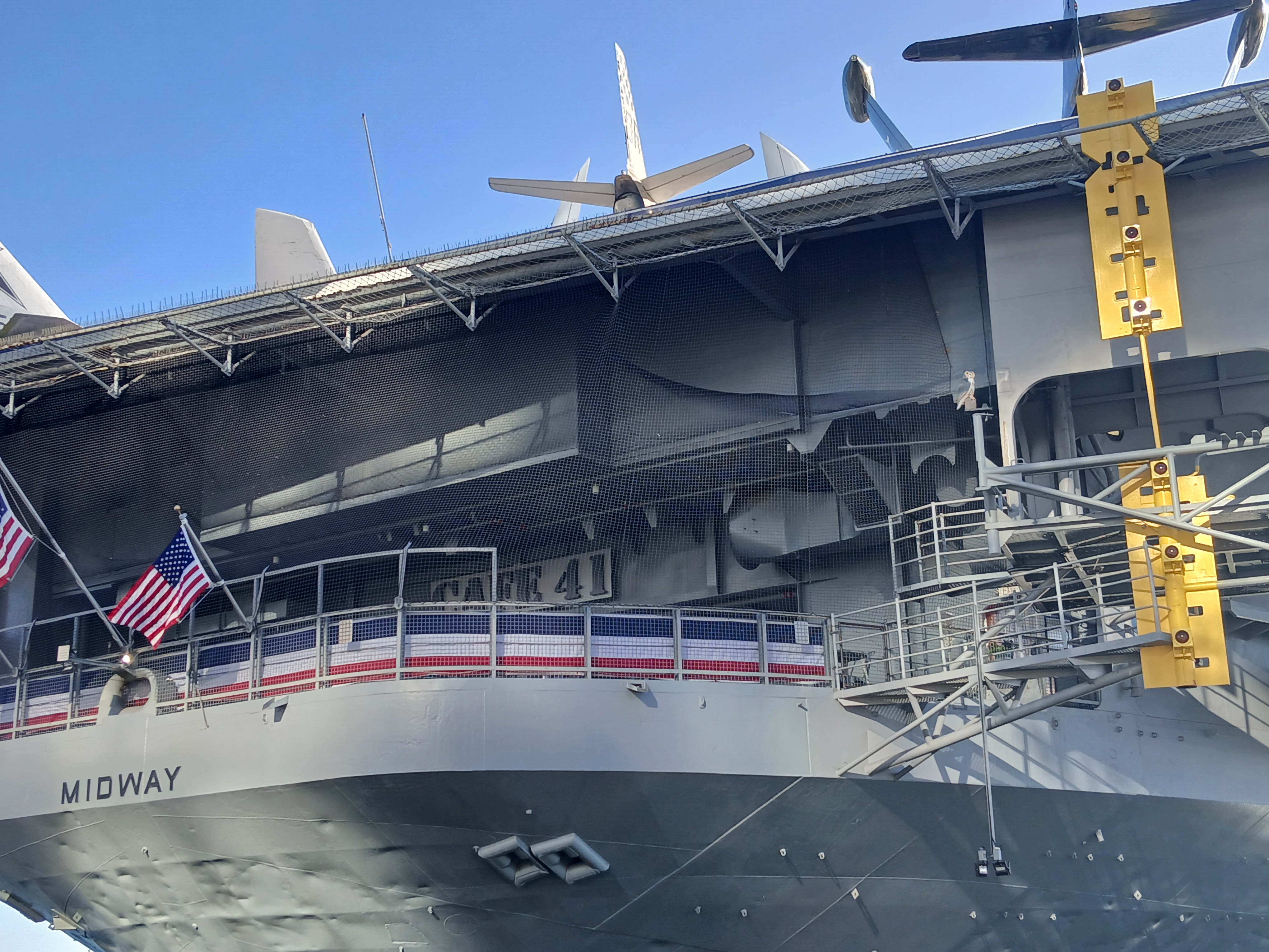 A view of the stern of the USS Midway, a dull exterior with dark letters saying MIDWAY painted on it.