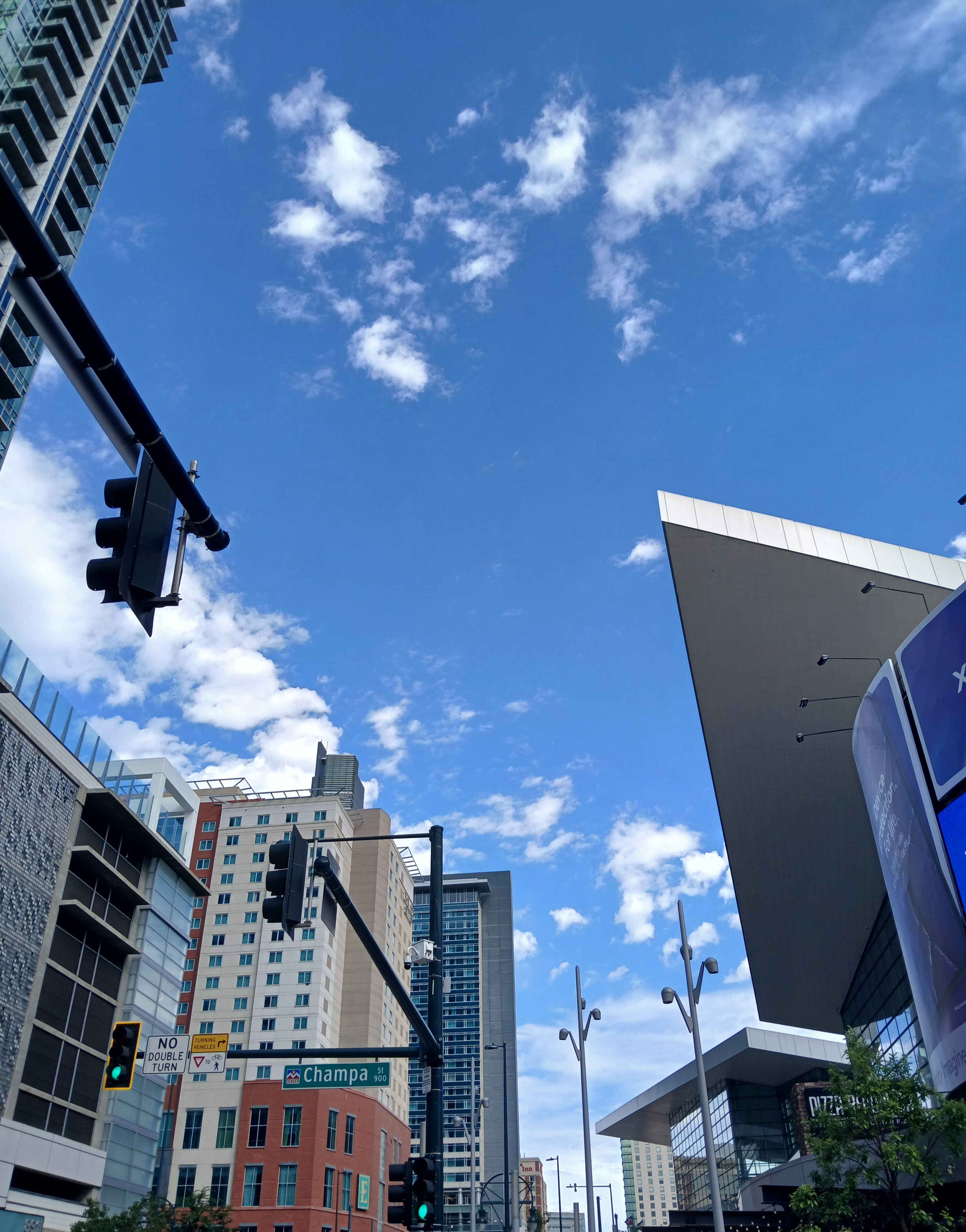 Highrise buildings standing on the left of streetlights and streetlamps with the overhanging roof and tall glass facade of the Colorado Convention Center looming to the right.