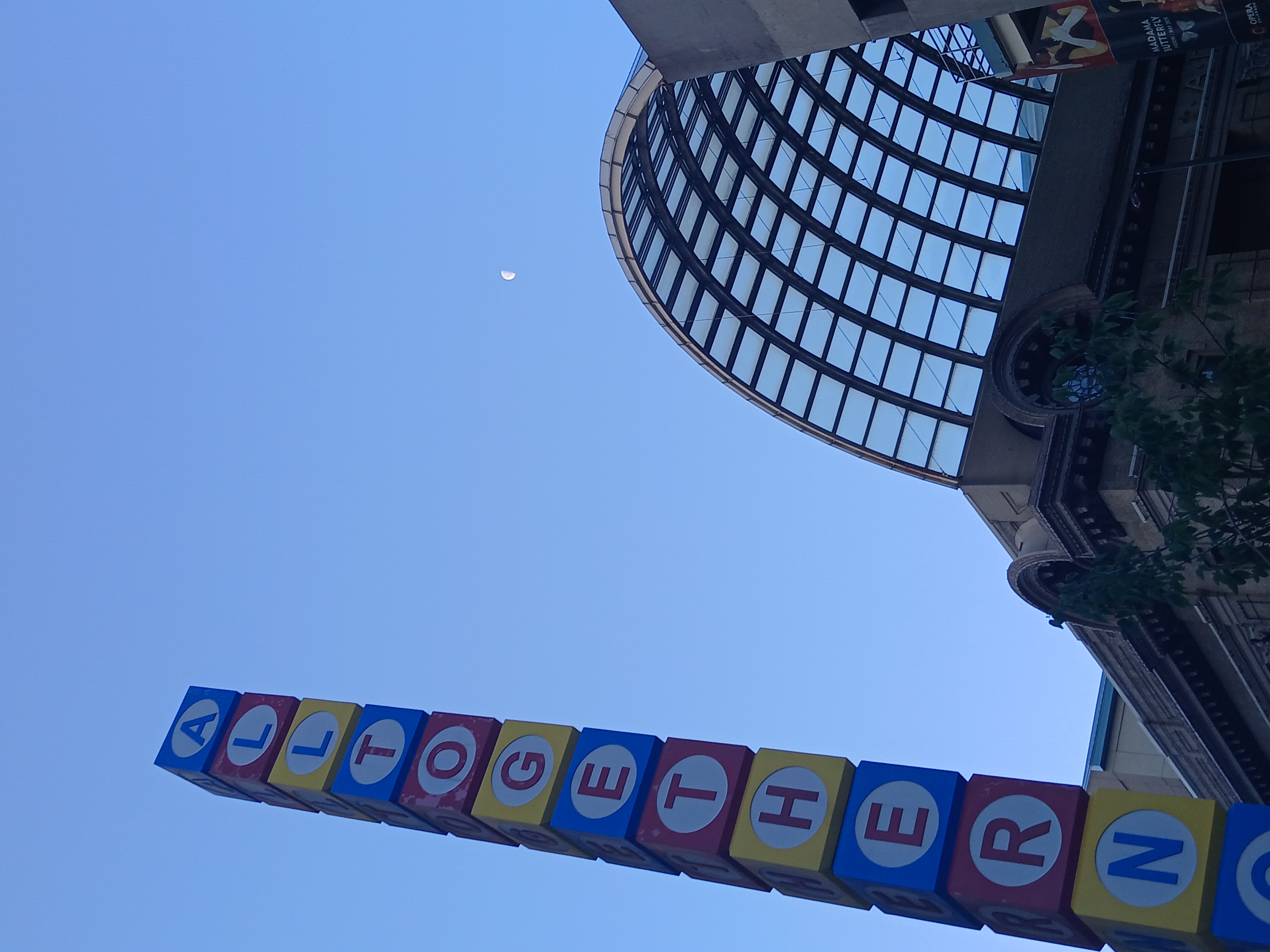 An odd statue, a segmented pillar, that stands on the corner of 14th and Curtis Streets in Denver Colorado. Its block-like segments read "ALL TOGETHER NOW"